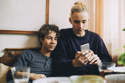 Young man looking through smart phone while sitting on laptop