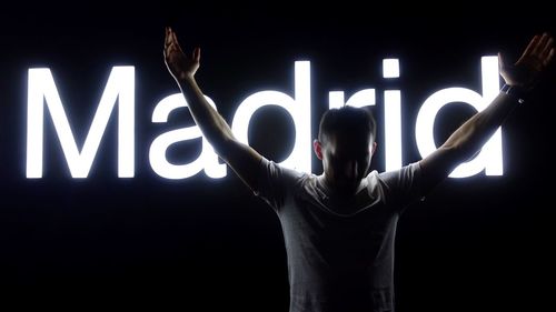 Man with arms raised standing against illuminated text on wall at night