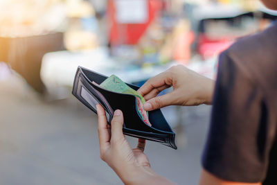 Close-up of woman holding removing money from wallet outdoors