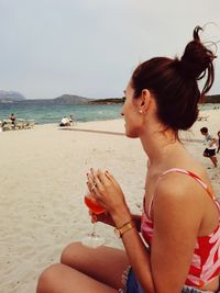 Woman sitting on beach by sea against sky