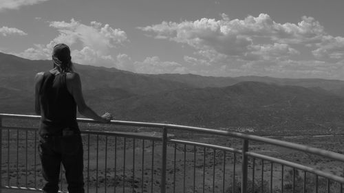 Rear view of person standing on railing against a valley