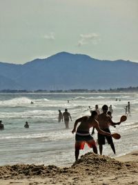 People playing at beach against sky on sunny day