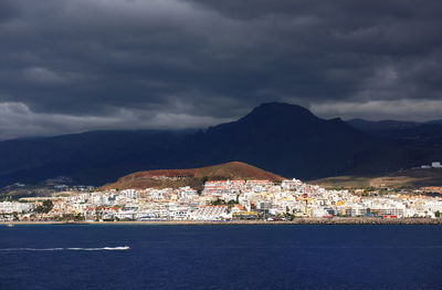 Sea and community by mountains against cloudy sky