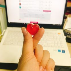 Close-up of hand holding heart shape candy by laptop