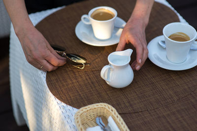 Cropped hands with sunglasses by milk in jar and coffee cups on table 