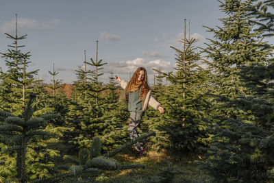 Happy girl with arms outstretched standing amidst fir tree farm