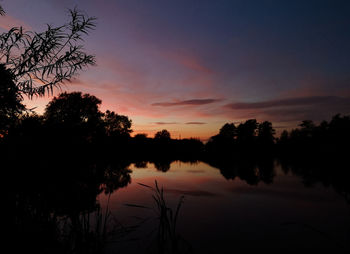 Silhouette trees by lake against romantic sky at sunset