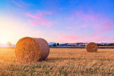 Hay bales on field against sky during sunset