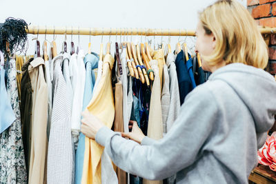 Woman shopper chooses fashionable clothes on hangers in a boutique.