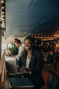 Portrait of smiling female entrepreneur sitting with laptop in hotel lounge