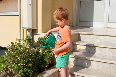 A blond boy watering flowers from a watering can. a four-year-old boy tends to flowers. 