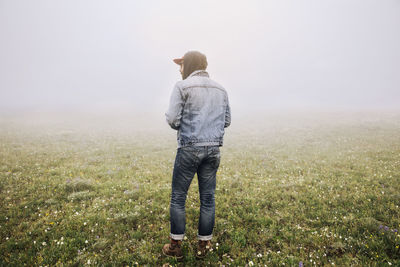 Rear view of man standing on field in foggy weather