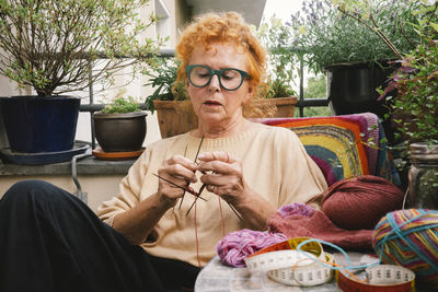 Elderly woman knitting sweater while sitting in balcony