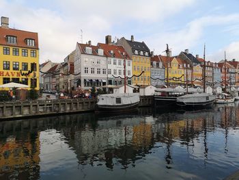 Sailboats moored on river by buildings against sky