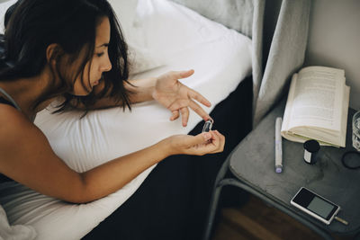 Woman checking blood sugar level while lying on bed