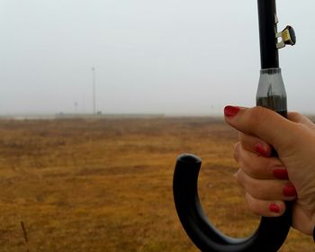 Close-up of person holding camera on field against sky