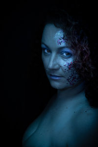 Close-up of woman with face paint against black background