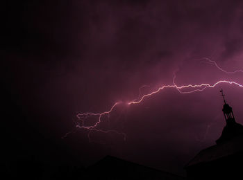 The bell tower of a church with a beautiful lightning crossing the sky, against plunged