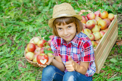 Portrait of girl holding apple sitting against crate