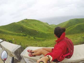 Rear view of woman sitting on mountain against sky