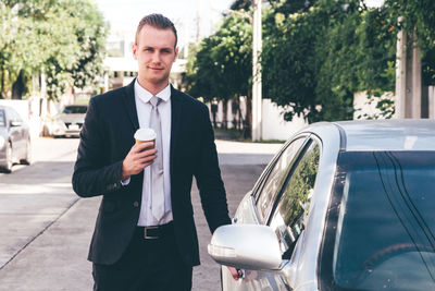 Portrait of businessman standing with car on road