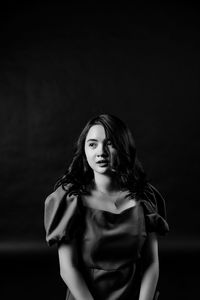 Portrait of young woman standing against black background