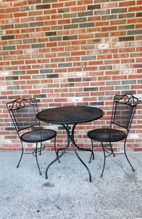 Empty chairs and table against brick wall