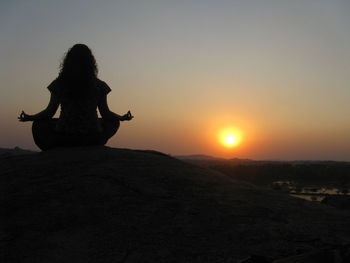 Silhouette woman sitting on rock against sky during sunset