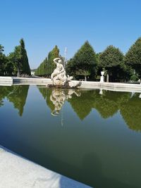 Reflection of sculpture in lake against clear sky