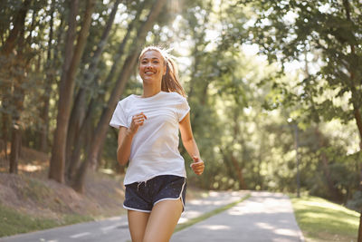 Full length of smiling young woman against trees