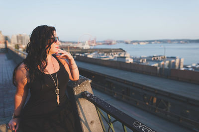 Thoughtful woman leaning on railing against sky