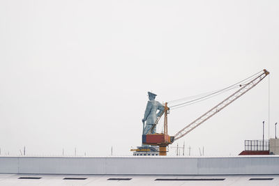 Low angle view of crane by building against clear sky