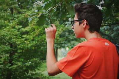 Side view of young man looking at leaf on branch at park