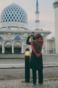 Rear view of woman photographing mosque with smart phone from footpath
