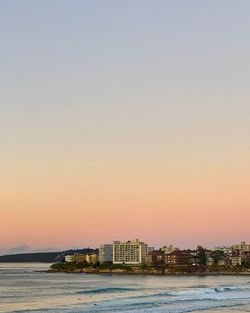 Sea by buildings against clear sky during sunset