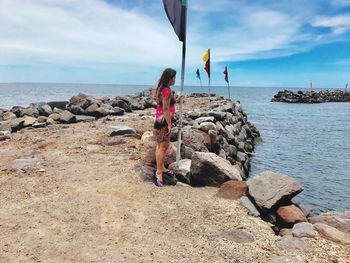 Full length side view of woman standing by flag and sea against sky