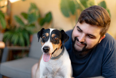 Friendly young man hugging his cute grocer dog while looking at him, the dog has the tongue out