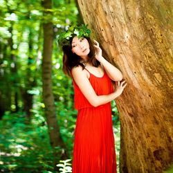 Beautiful young woman looking away while standing by tree trunk in forest