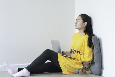 Young woman looking away while sitting on wall at home