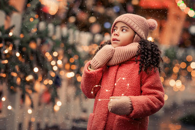 Portrait of young woman standing against illuminated christmas tree