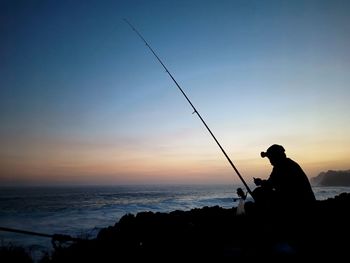 Rear view of man standing on sea against sky during sunset