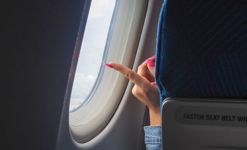 Cropped hand of woman pointing at window in airplane