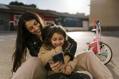 Smiling mother using mobile phone while sitting on road