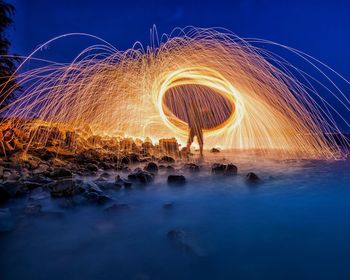 Person spinning wire wool by sea at night