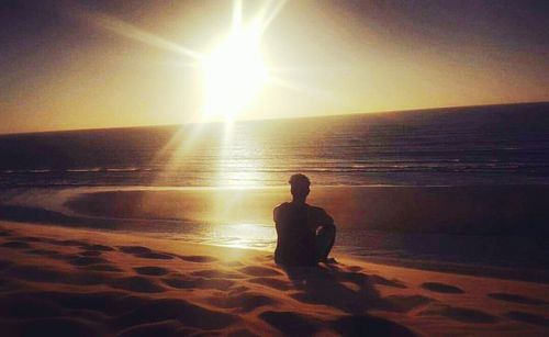Man sitting on beach at sunset