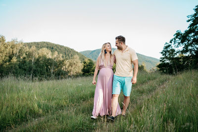 Boyfriend walking with pregnant girlfriend at park against clear sky