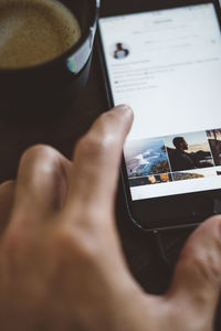 Cropped hand of man using smart phone by coffee cup on table at home