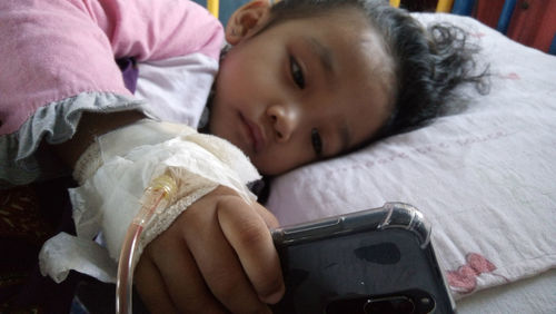 Cute injured girl using phone while lying on hospital bed