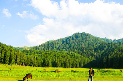 Mid adult man standing of green field against sky