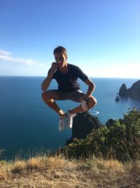 Full length of young man levitating over cliff against sea and sky